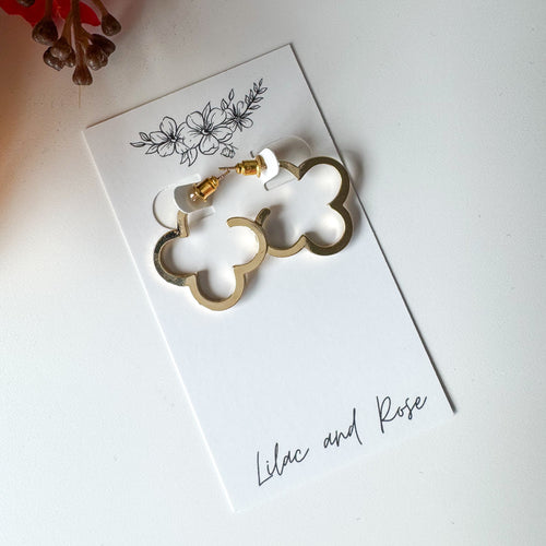 Gold clover-shaped earrings on a white card with 'Lilac and Rose' branding, on a light background.