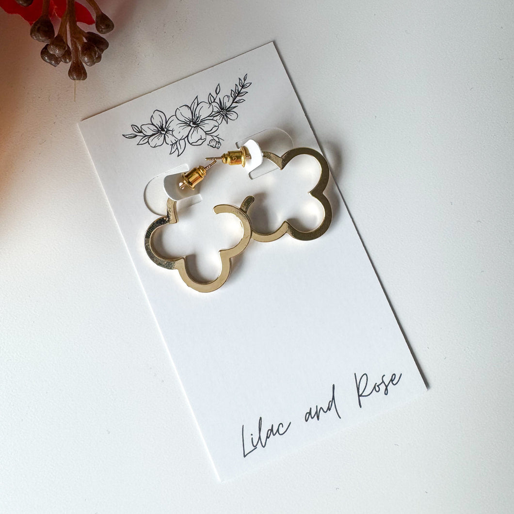 Gold clover-shaped earrings on a white card with 'Lilac and Rose' branding, on a light background.