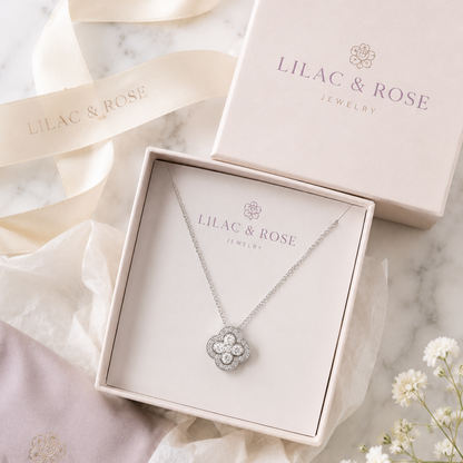 A silver-toned four-leaf clover pendant necklace by Lilac & Rose Jewelry, displayed in an open cream-colored gift box with its lid and ribbon nearby on a light marble surface.