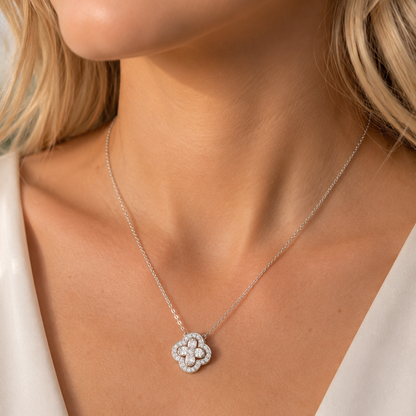 A close-up of a model wearing a delicate silver flower-shaped pendant necklace with clear stones, styled with a white top.