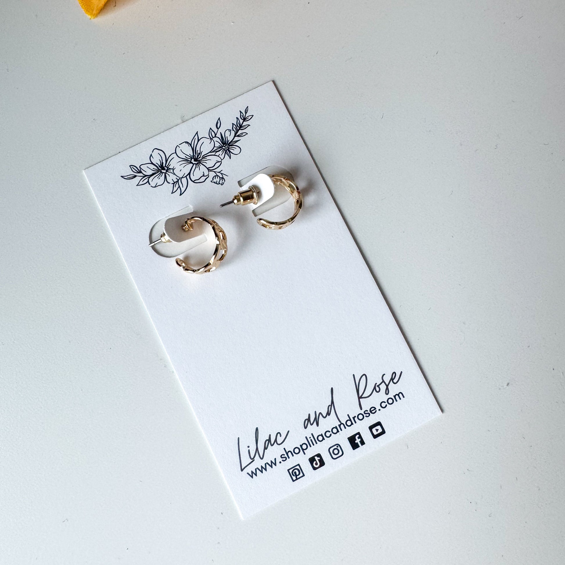 A pair of silver mini chain hoop earrings displayed on a white card with floral pattern and the brand name 'Lilac and Rose' written at the bottom.