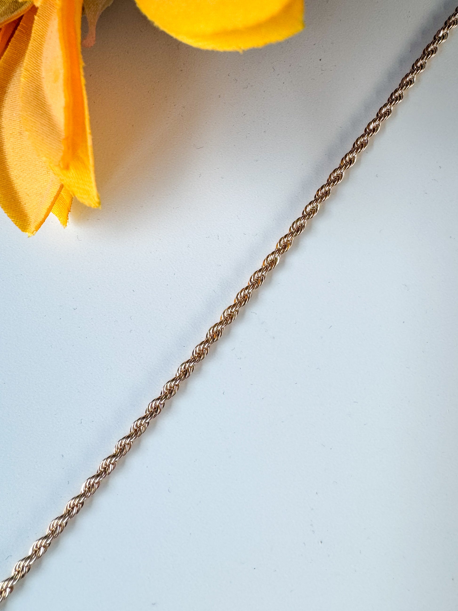 Gold chain on a white surface with a yellow flower