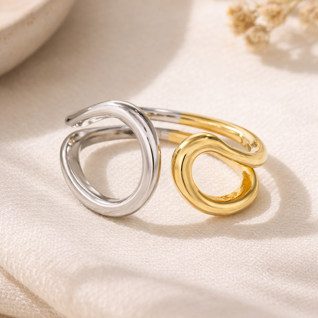 Two rings, one silver and one gold, on a soft beige fabric background.