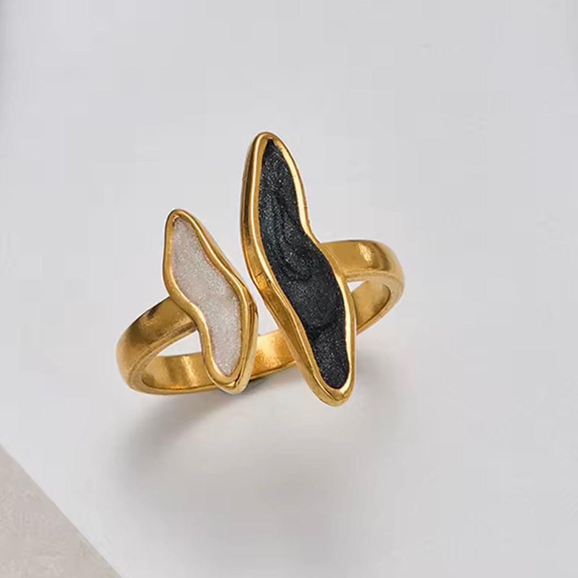 Gold ring with black and white stone on a light gray background
