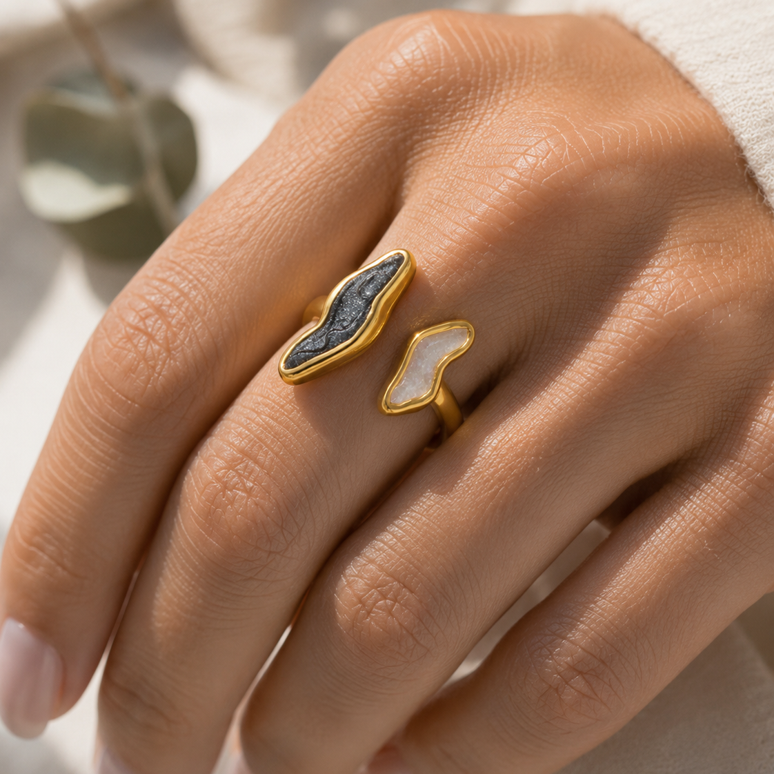 A close-up lifestyle shot of a woman in a cream knit sweater holding a gray marble mug, wearing a gold ring with a dark blue marquise-cut stone.