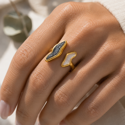 A close-up lifestyle shot of a woman in a cream knit sweater holding a gray marble mug, wearing a gold ring with a dark blue marquise-cut stone.