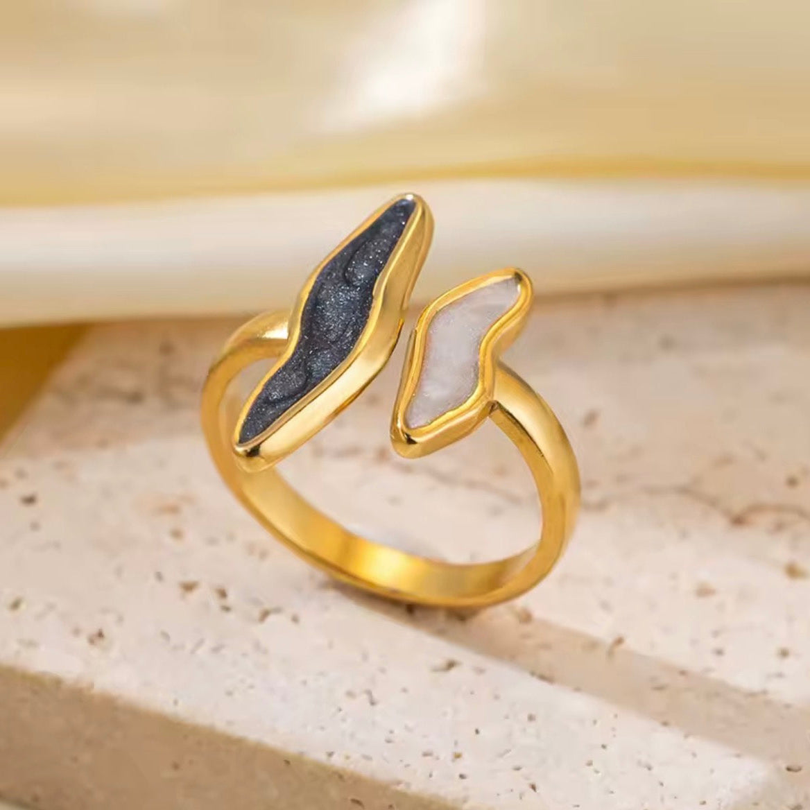 Gold ring with black and white stone inlays on a beige surface