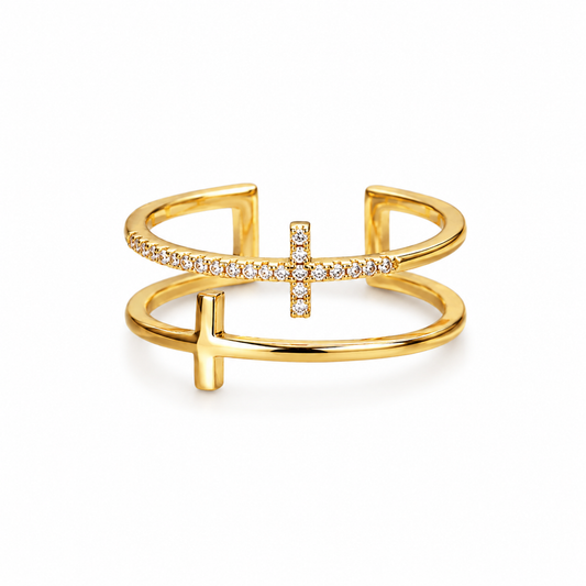 A gold open cuff ring featuring a central cross motif, one arm paved with small clear stones, and a polished cross protruding from the center, shown on a white background.