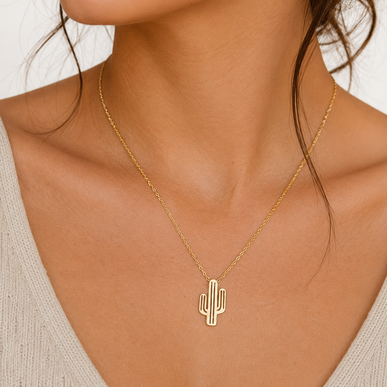 A gold cactus pendant necklace worn by a model, shown in a close-up shot of the neck and upper chest.