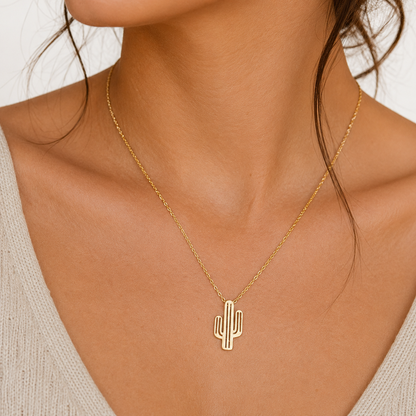 A gold cactus pendant necklace worn by a model, shown in a close-up shot of the neck and upper chest.