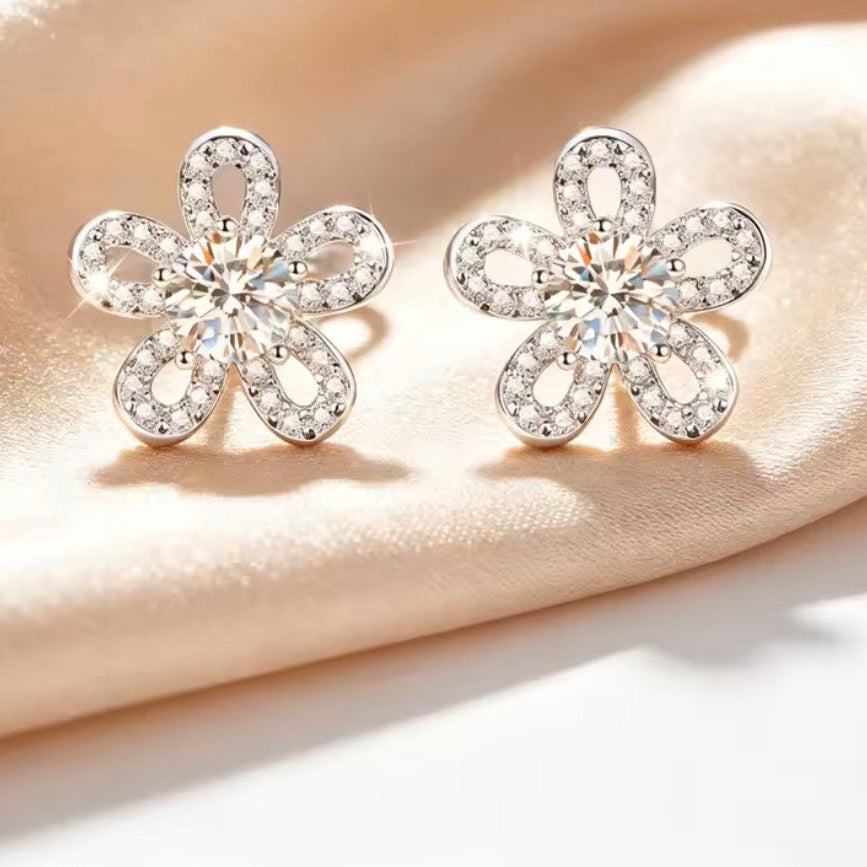 Flower-shaped silver earrings with clear moissanite stones on a beige fabric background