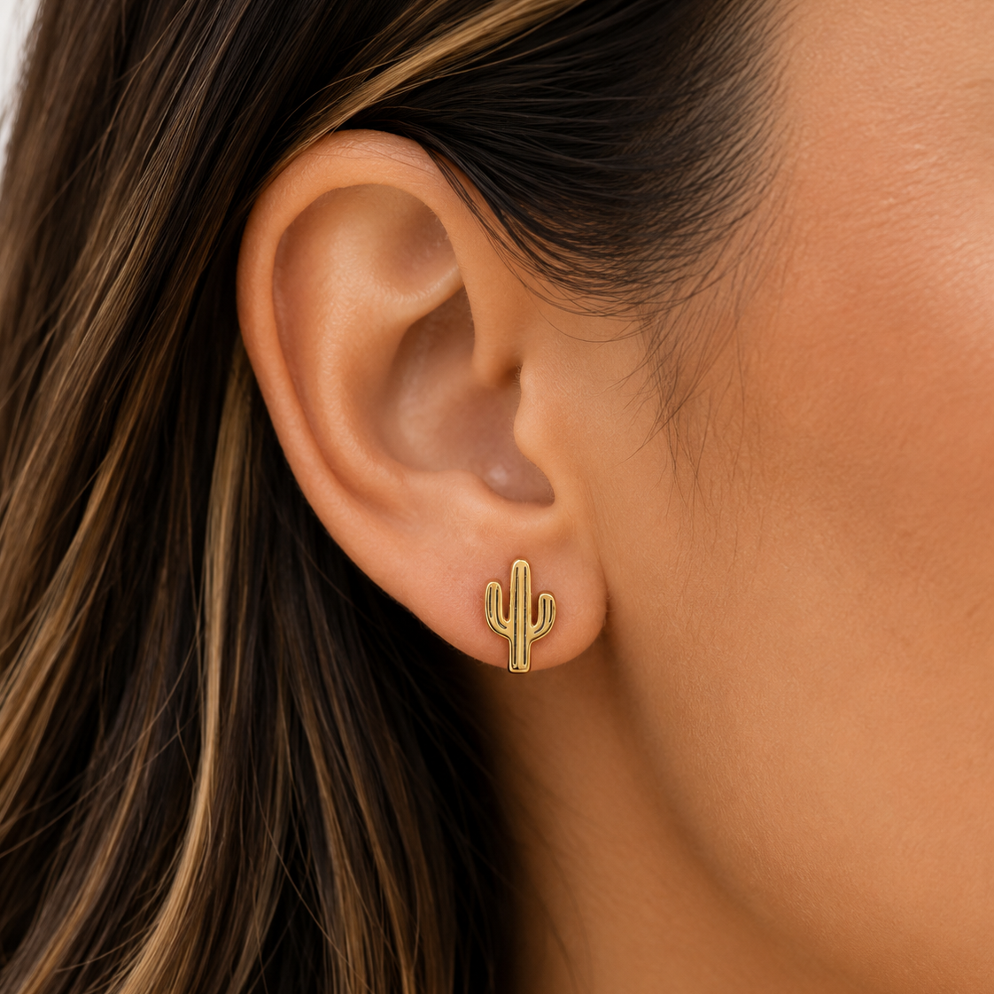 A close-up of a person's ear wearing a small gold cactus stud earring.