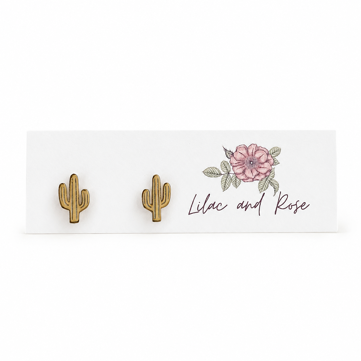 A pair of small gold cactus stud earrings displayed on a white card with a pink flower illustration and the script text 'Lilac and Rose'.