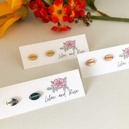 Stainless steel football stud earrings in silver and rose gold colors, displayed on a white card with a floral design and the words 'Lilac and Rose' written on it.