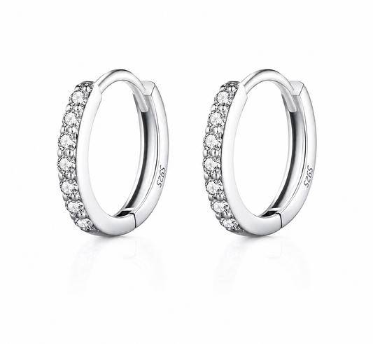 A pair of silver huggie hoop earrings with a row of clear pavé-set round stones on the front, shown on a clean white background with a soft reflection.