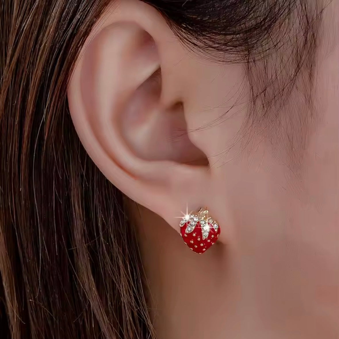 Close-up of an ear wearing a red strawberry-shaped earring with gold accents.