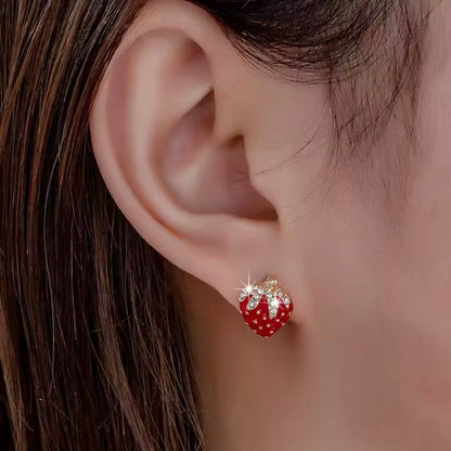 Close-up of an ear wearing a red strawberry-shaped earring with gold accents.